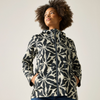 A woman wearing a hooded zip-up jacket with a bold black and off-white floral pattern, standing against a plain light gray studio background.