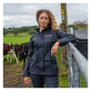 Woman in a navy jacket standing in a field with cows and a fence.