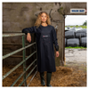 Woman in a navy blue apron standing in a farm setting with a 'Wash Bay' sign in the background.