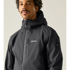 A man wearing a dark gray hooded technical jacket with a zippered chest pocket and a small white logo on the chest, photographed against a plain light beige studio background.