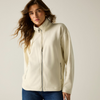 A woman wearing a cream-colored zip-up jacket with a mock neck and side pockets, paired with blue jeans, photographed against a neutral light beige background.