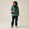 Person wearing a green jacket and dark pants, holding a purple bag on a beige background