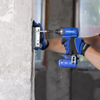 A person wearing blue and black gloves uses a blue and black Frunkidrive cordless drill to install a metal bracket onto a concrete wall.