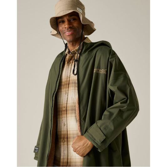 A man wearing an olive green hooded raincoat over a brown and beige plaid flannel shirt, paired with a beige bucket hat, against a solid light gray background.