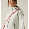 A woman wearing a light gray hooded jacket with a pink crossbody strap, photographed against a plain light beige studio background.