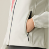 Close-up of a person wearing a light off-white zip-up jacket, with a hand tucked into a side pocket. The jacket has a dark zipper trim and a small pink accent near the shoulder.