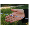 A close-up of a person's hand holding a thin twisted rope or cord that is blue and white, with a blurred outdoor grassy background.