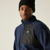 Man wearing a navy fleece jacket with a black zipper and black beanie on a beige background