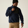 Man wearing a navy fleece pullover with a brand logo on a beige background