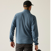 A man shown from behind wearing a slate blue fleece pullover and a black baseball cap, photographed against a plain light beige studio background.