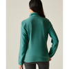 A woman shown from the back wearing a teal green long-sleeve fleece pullover and dark gray leggings against a solid light beige background.