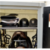 An equestrian tack storage cabinet with a glass door, showing folded black and white cloths, two black riding helmets, a brown leather saddle, and hanging black bridles.