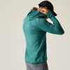 A man wearing a teal long-sleeve hooded athletic jacket, shown from the back and side as he adjusts the hood. He is also wearing a black baseball cap and gray pants, photographed against a plain light beige studio background.