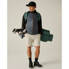 A man modeling a slate blue quilted puffer vest over a black long-sleeve shirt, paired with beige golf shorts, black golf shoes, and carrying a green golf bag and gloves on a light gray studio background.