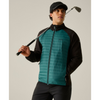 A man wearing a teal and black zip-up puffer jacket, black pants, and a black cap, holding a golf club against a plain beige studio background.