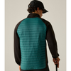 A man viewed from behind wearing a teal and black quilted puffer vest over a black long-sleeve shirt and a black cap, holding a golf club against a plain beige studio background.