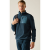 A man wearing a navy blue quarter-zip fleece pullover with a contrasting light blue chest pocket, paired with matching navy pants and carrying a black backpack, set against a plain light gray background.