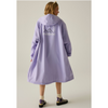 A model is shown from the back wearing a light purple hooded raincoat with a white mountain graphic and text printed on the back. The background is a solid, warm off-white studio backdrop.