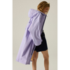 A model wearing a light purple hooded raincoat, shown from a side-back angle against a plain beige studio background.