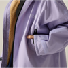 Close-up of a lavender outdoor jacket with a tan fleece lining, black zipper, and a side pocket being opened, with a finger visible.