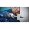 A close-up action shot of a man using a blue cordless drill to install a blue wall anchor into a wooden block set against a concrete wall.