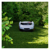 Robotic lawn mower on a grassy area with bushes in the background