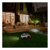 Robotic lawn mower on grass in a modern outdoor setting with pool and patio.