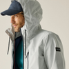 A man wearing a light gray hooded jacket with black drawstrings, a navy baseball cap, and a teal shirt underneath, shown in a close-up side profile against a plain light beige background.
