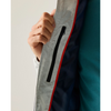 Close-up of a person's hand holding open a light gray zippered jacket, showing a black zipper pocket, a red piping accent, and a dark navy interior lining next to a teal shirt.