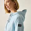 A woman wearing a light blue hooded jacket, shown in a close-up side profile against a plain light background. A black rectangular sleeve patch on the jacket shown