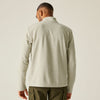 Man wearing a beige fleece pullover and green pants on a plain background