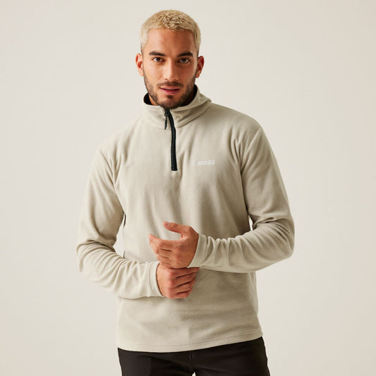 Man wearing a beige pullover with a brand logo on a plain background