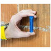 A hand holding a blue plastic wall anchor insert against a textured orange-brown brick wall.