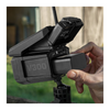 A close-up of a black V300 camera or monitor rig being adjusted by a person's hand, with an antenna and mounting hardware visible against an outdoor blurred background.