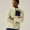 A man wearing a cream-colored fleece pullover with a navy blue chest pocket and zipper, posed against a solid light gray background.