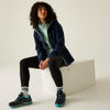 Person wearing a navy jacket, light green shirt, black leggings, and teal sneakers sitting on a white block.