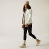 Woman wearing a white jacket, black leggings, and beige sneakers on a plain background