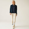 Woman wearing a navy jacket, black top, cream leggings, and white sneakers on a beige background