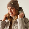 Woman wearing a brown knit beanie and beige jacket against a neutral background