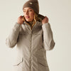 Woman wearing a beige winter coat and beanie on a light background