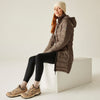 Woman wearing a brown puffer coat, black leggings, and beige sneakers sitting on a white block.