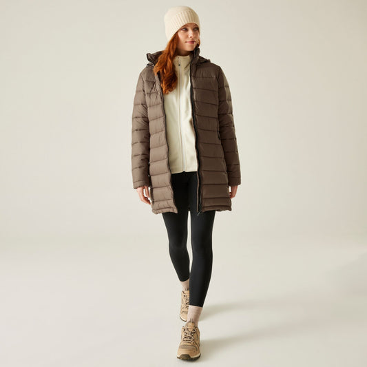 Woman wearing a brown puffer coat, white beanie, black leggings, and beige boots on a light background