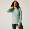 Woman wearing a light green pullover with a brand logo on a plain background