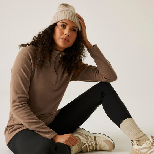 Woman wearing a brown long-sleeve top, black leggings, and beige beanie sitting on the floor.