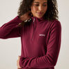 Woman wearing a maroon pullover with a logo on a plain background