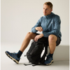a man sitting on a white block, holding a backpack, wearing the blue jacket and blue shoes
