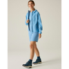 A woman modeling a blue zip-up jacket, blue shorts, black socks, and hiking boots, set against a plain light beige studio background.