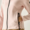 A close-up of a blonde woman wearing a light pink mock-neck long-sleeve top, pulling the zipper tab to show the front closure.