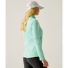 A woman wearing a light mint green long-sleeve athletic top, black leggings, and a white baseball cap, shown from a side-back angle against a plain light gray studio background.