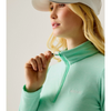 A woman wearing a mint green long-sleeve quarter-zip pullover and a white visor, shown in a close-up profile against a light gray studio background.